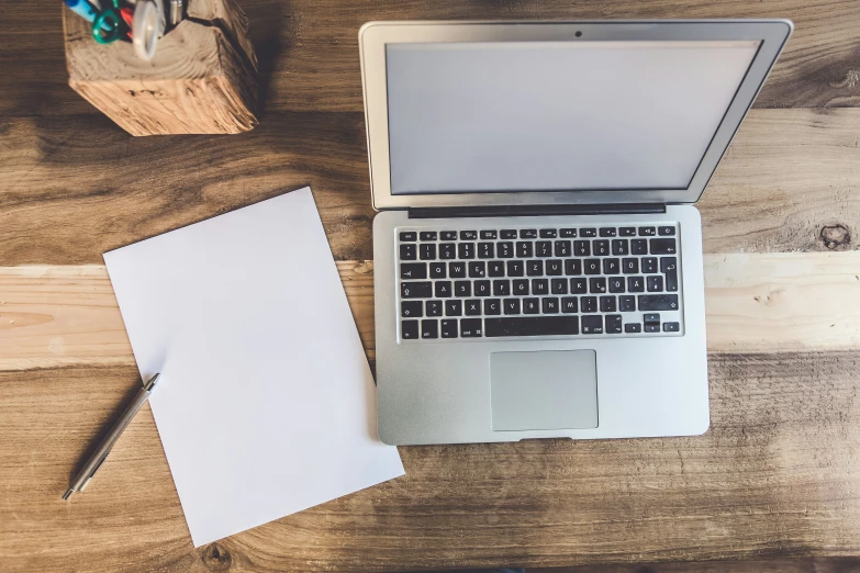 a laptop, notepad and pen on top of a wooden table