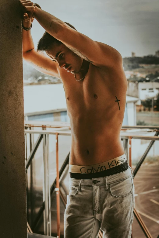 a shirtless man with cross tattoos is standing by railing