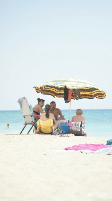a group of people sitting around a beach with an umbrella