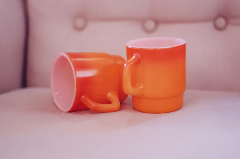 an orange mug sitting next to another orange mug