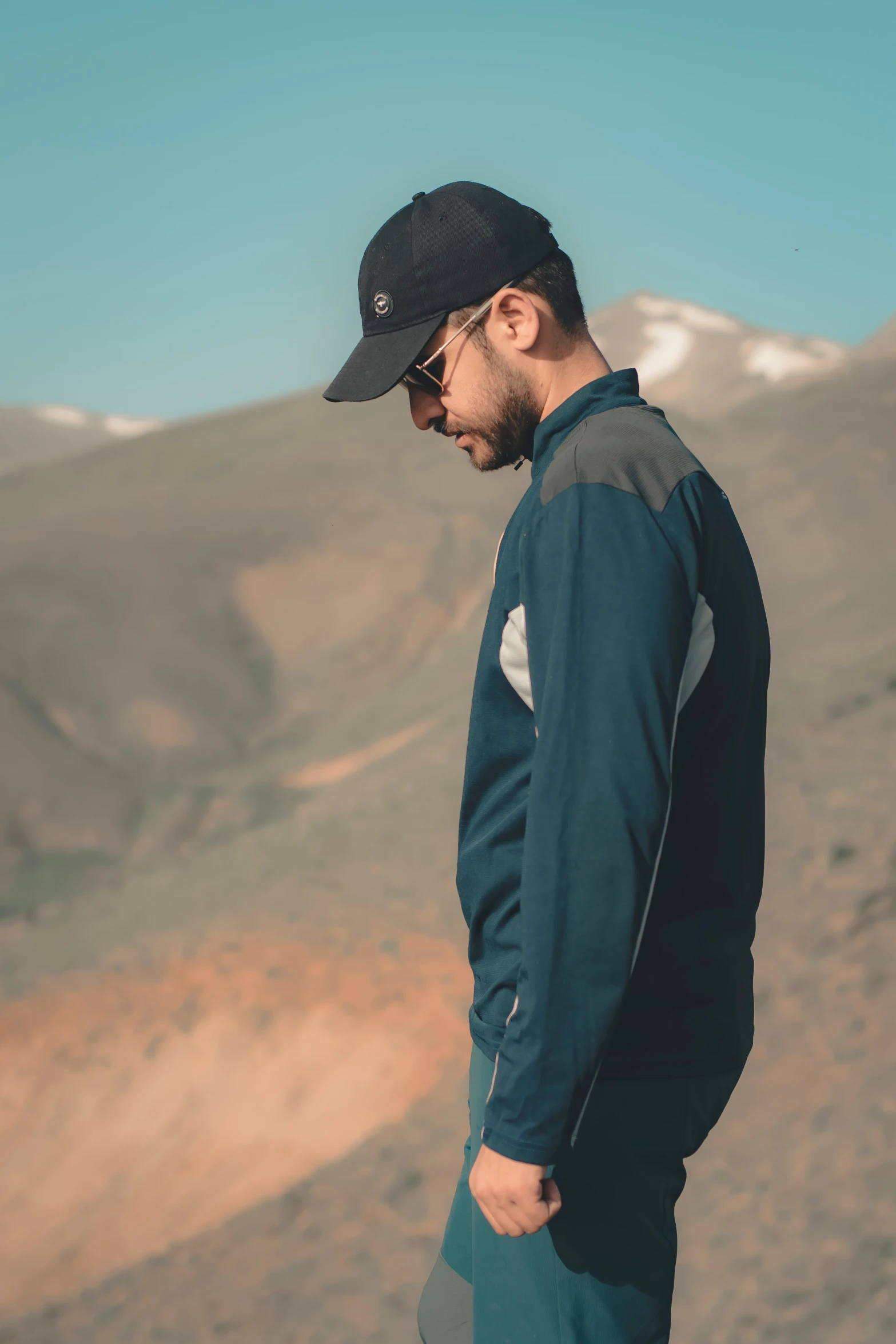 a man standing in the mountains wearing a black hat