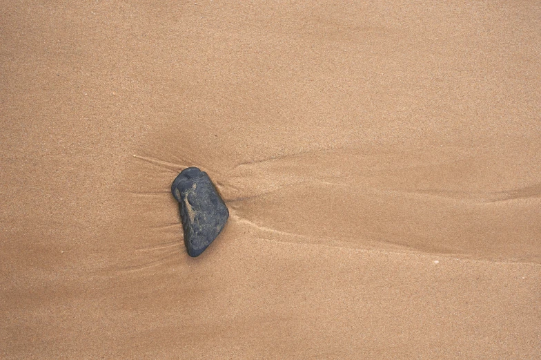 a small blue rock sits in the sand on the beach