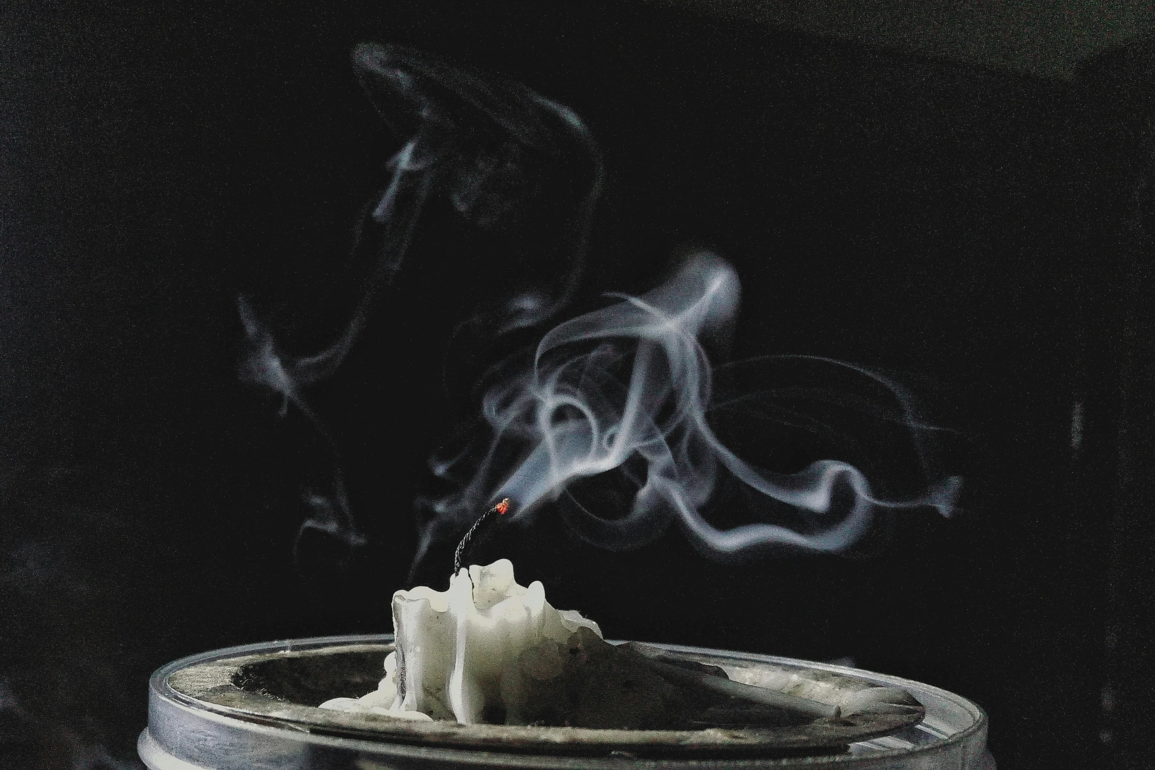 a single candle in a silver bowl with smoke coming out of the top