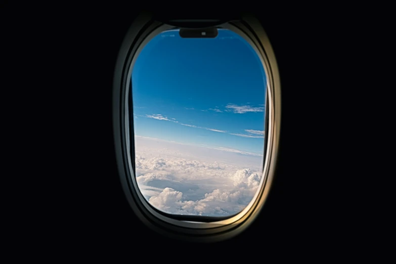 an airplane window showing a bright blue sky and clouds
