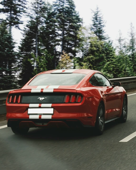 a red sports car drives down a road with trees in the background