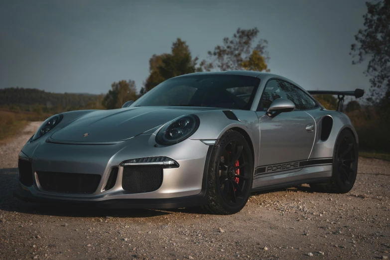 silver sports car sits on dirt with trees in background