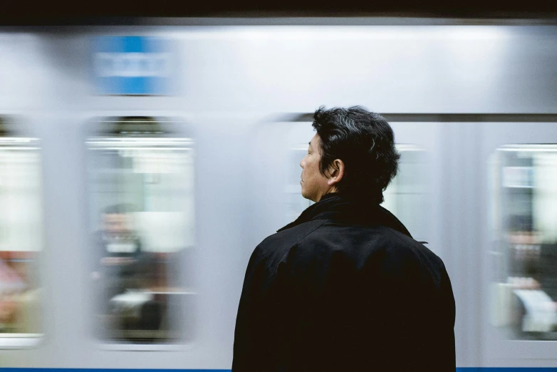 a man in black shirt next to train and white wall