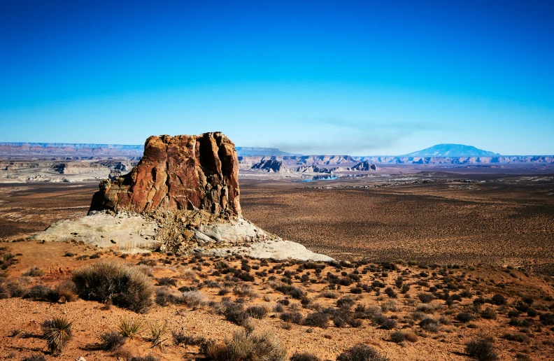 a desert landscape with a rock in the middle and a mountain range in the background