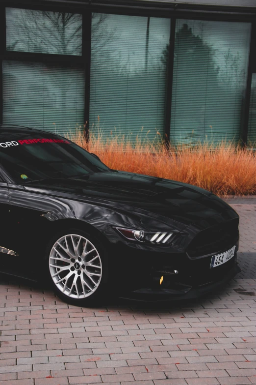 a dark colored sports car parked in front of a glass building