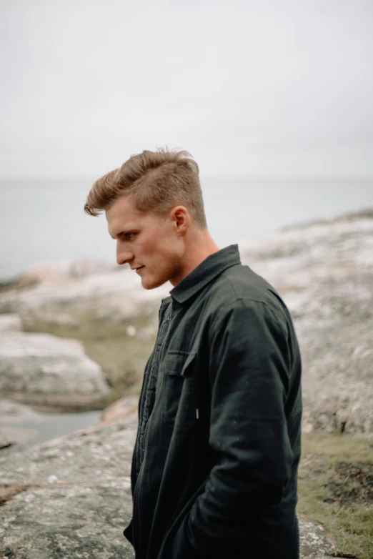 a man with a messy short hair stands on a rocky cliff