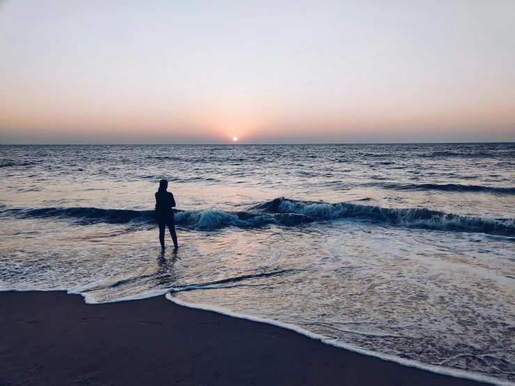 the person walks through the ocean at sunset