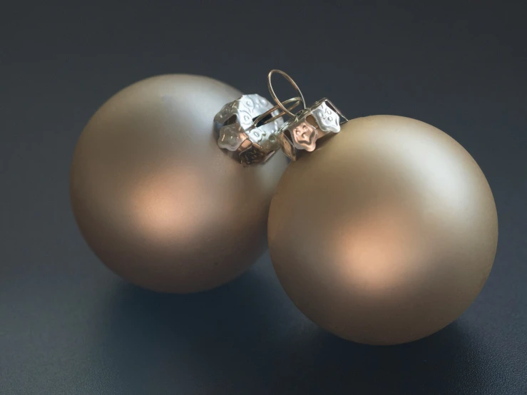 two gold christmas ornaments hang on a black background
