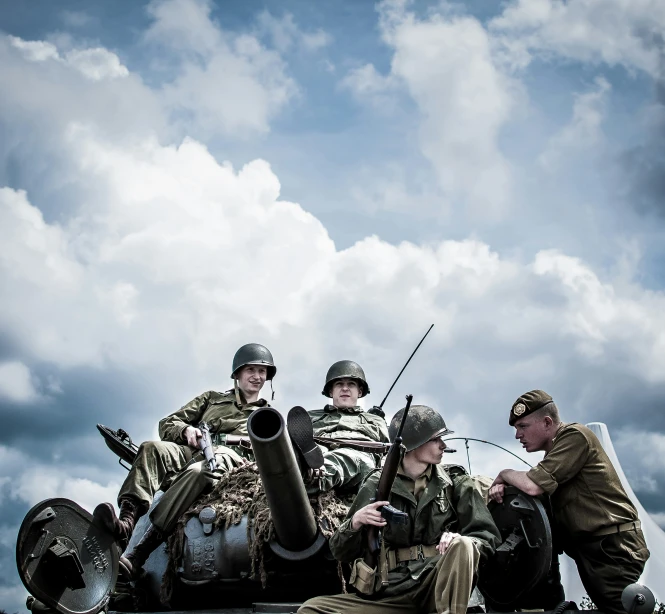 three men sitting in front of a tank, one with guns