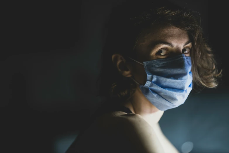 a woman wearing a surgical mask against a dark background