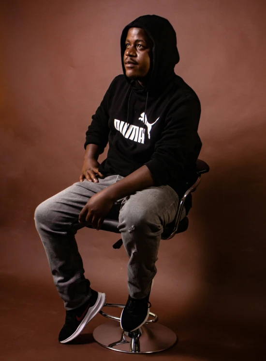 a man sitting on a stool wearing black and white clothing