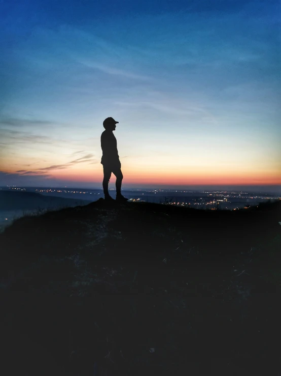 a person on a mountain top at dusk, with a hat