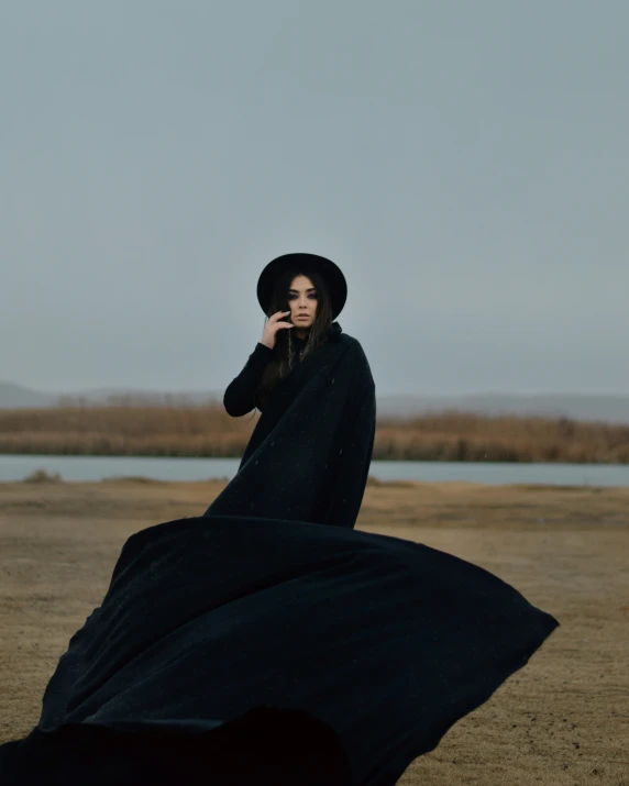 a woman in a long dress and hat is standing in the sand