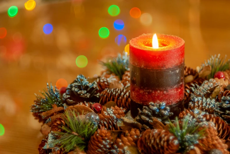 a christmas candle and pine cones with christmas lights in the background