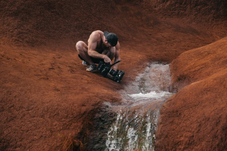 a man kneeling by a stream with his skateboard