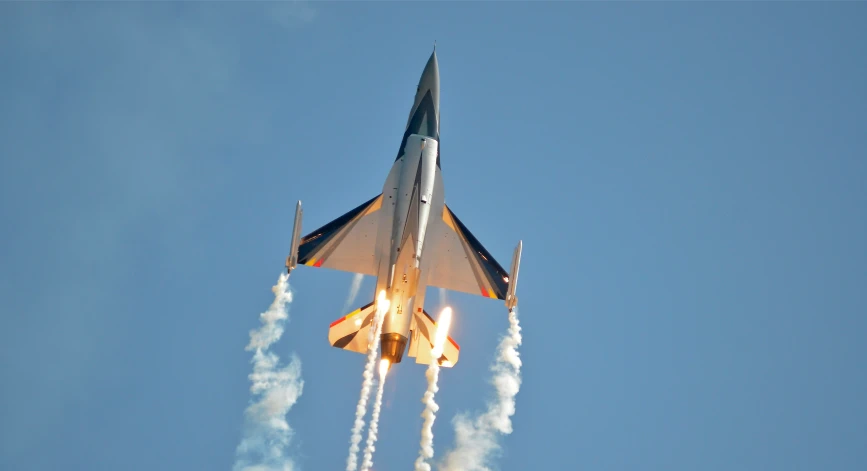 a jet flying through a blue sky with two smoke trails