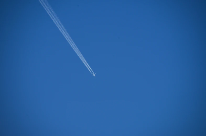 an airplane in the sky with contrails against a blue sky