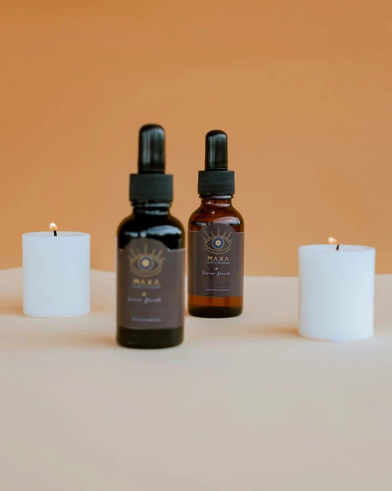 two bottles of oils and one of the candles is in front of an orange wall