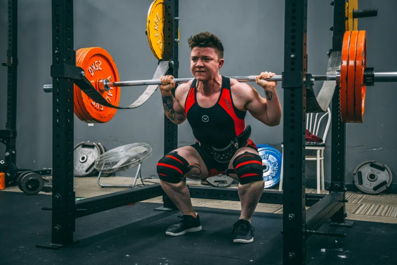 man squatting with a barbell on a bench in a gym