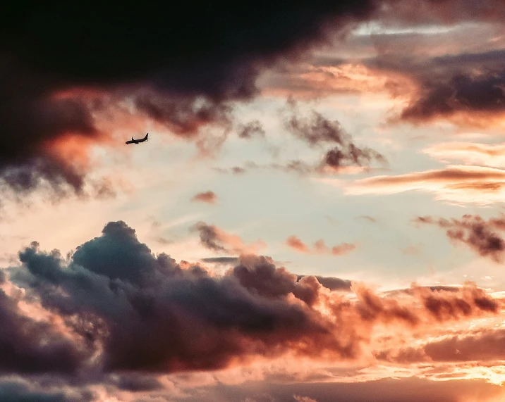 a jetliner flying through a cloudy sky under a purple and red cloud