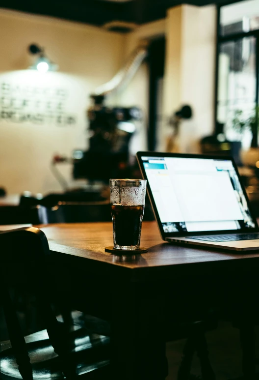 a glass with some drink next to a laptop