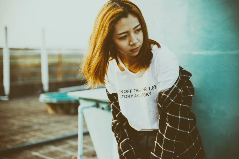 an asian young lady wearing a jacket while leaning against a wall