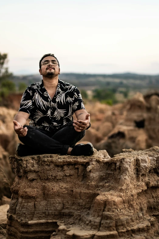 a man meditates on a rock in a place with trees