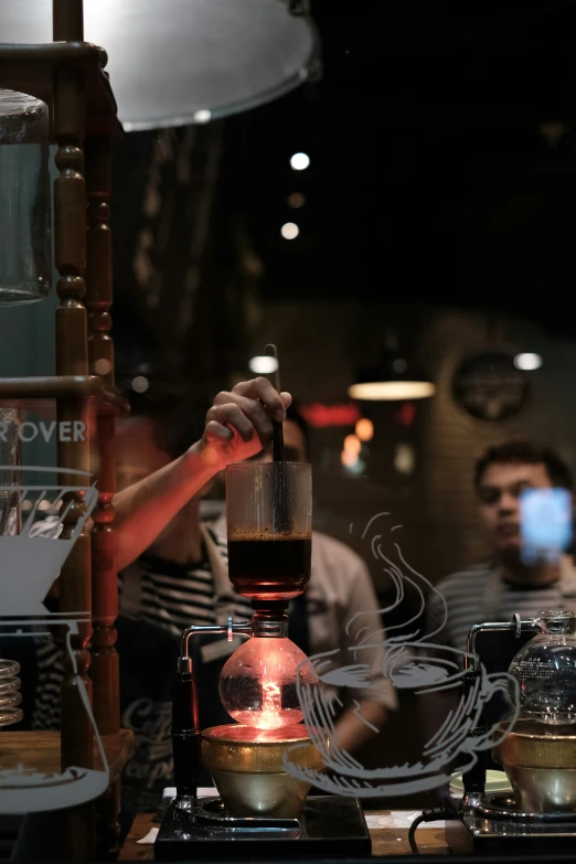 a glass making liquid on a stove while two men watch