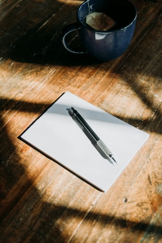 a pen is sitting on a piece of paper, next to a mug