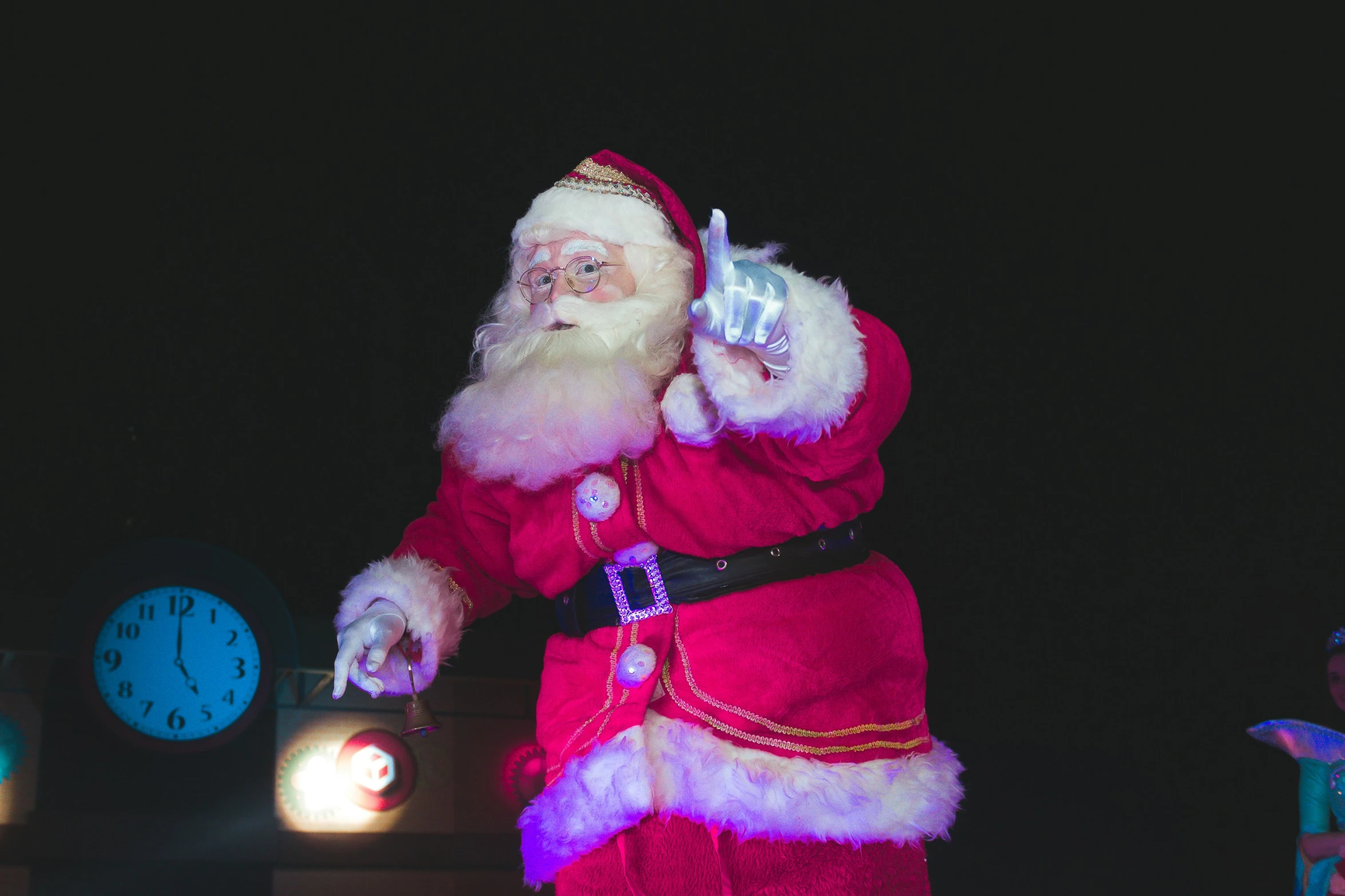 a santa is making a gesture in front of a clock