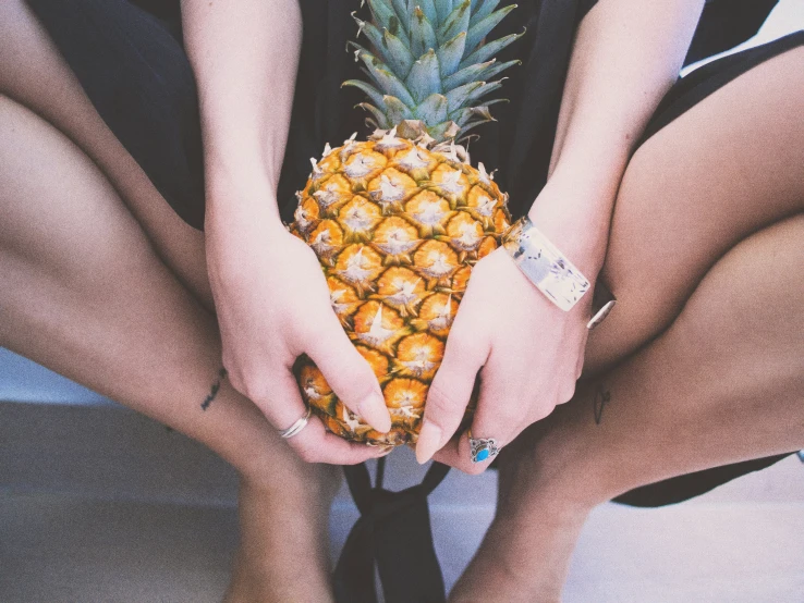 a close up of a person's hands holding an unpeeled pineapple