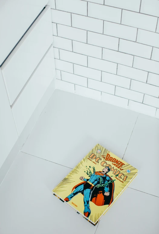 a dc comics book sits on the floor in front of a white brick wall