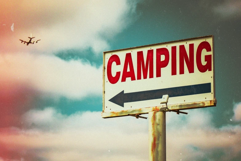 there is a white sign that says camping under a cloudy sky