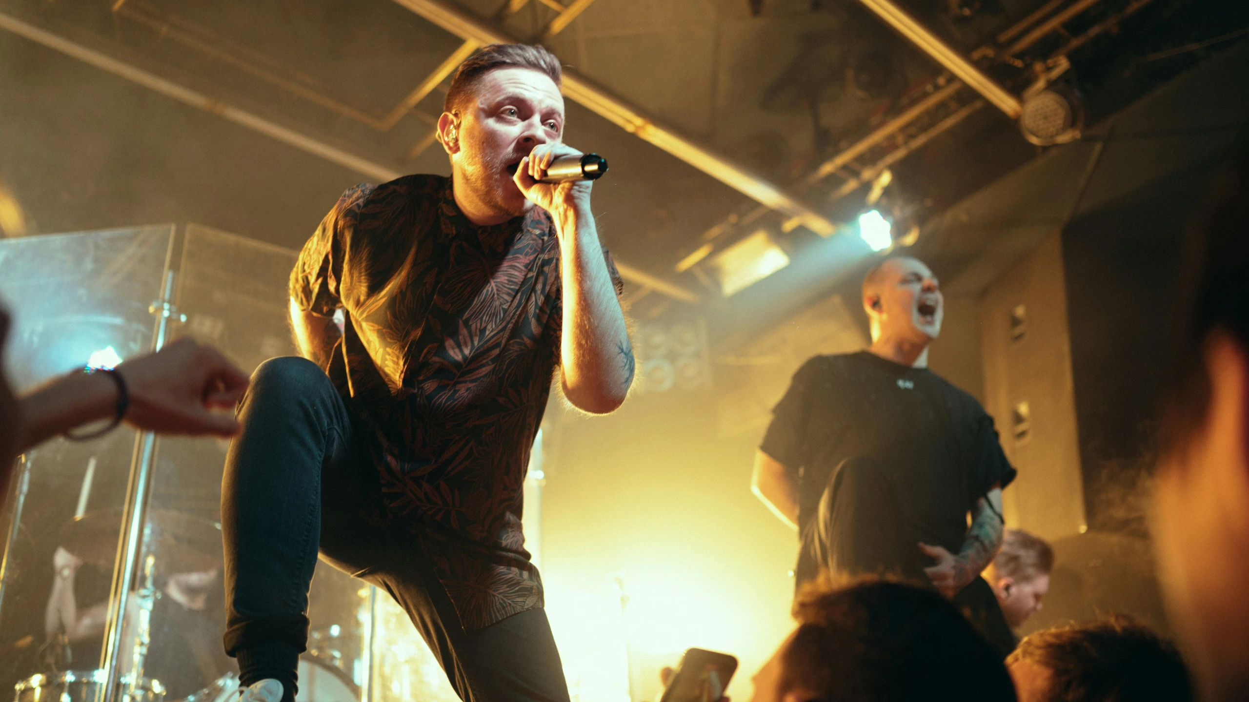 a man on stage singing into microphones to a group of people