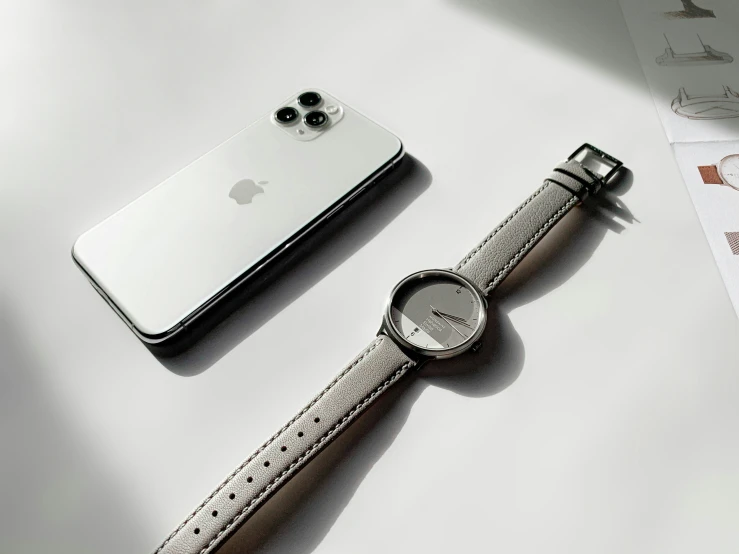 a silver watch on a leather strap is near an apple phone