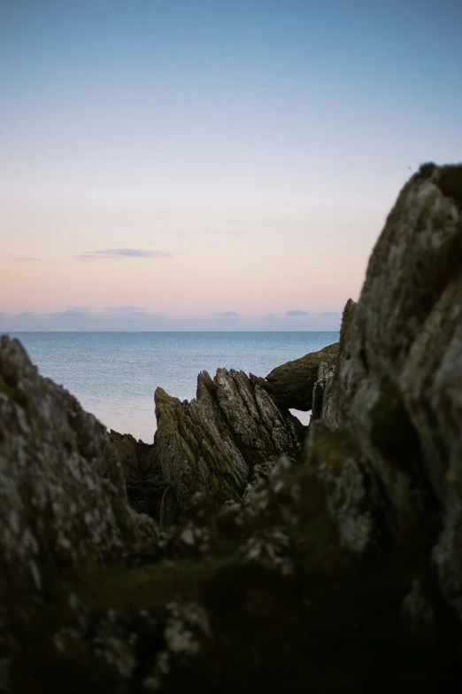 a rock in front of the ocean with a person sitting on top