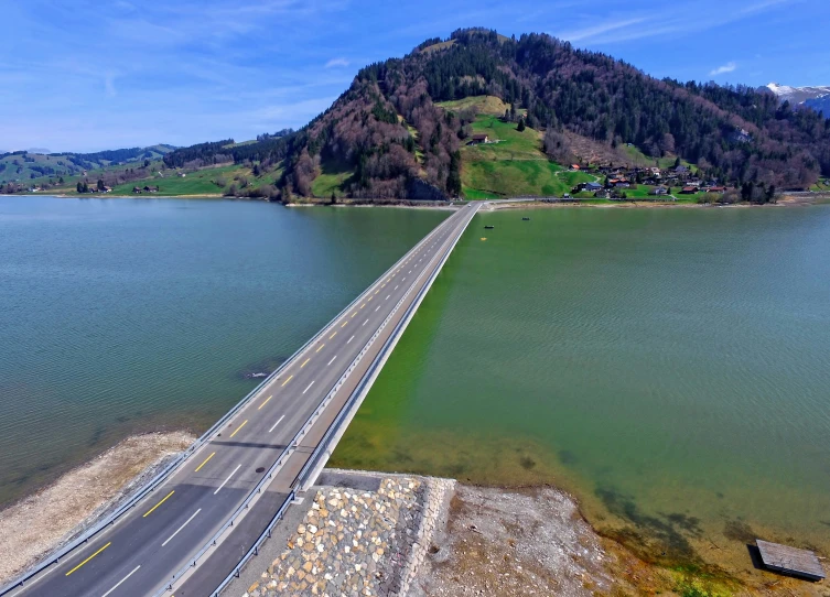 an aerial po of a road near water with a large mountain in the background