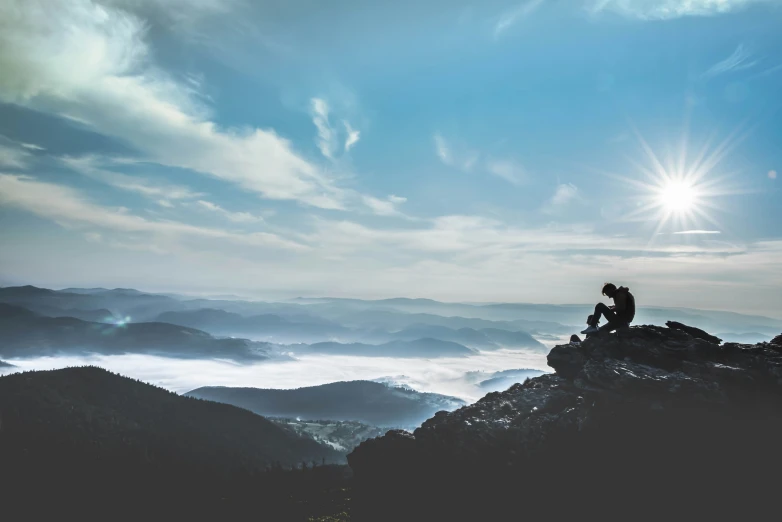 a person is sitting on a hill above the clouds