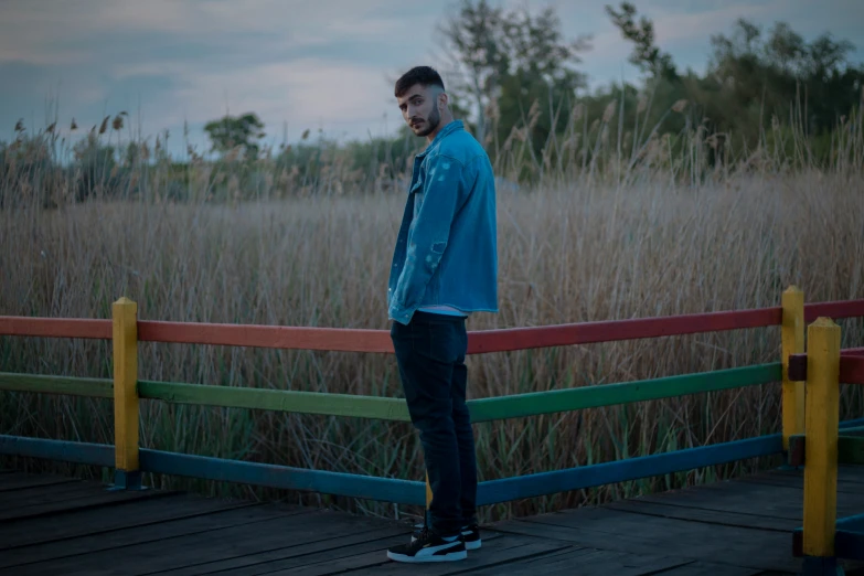 a man leaning on the railing of a wooden boardwalk with tall grass behind him