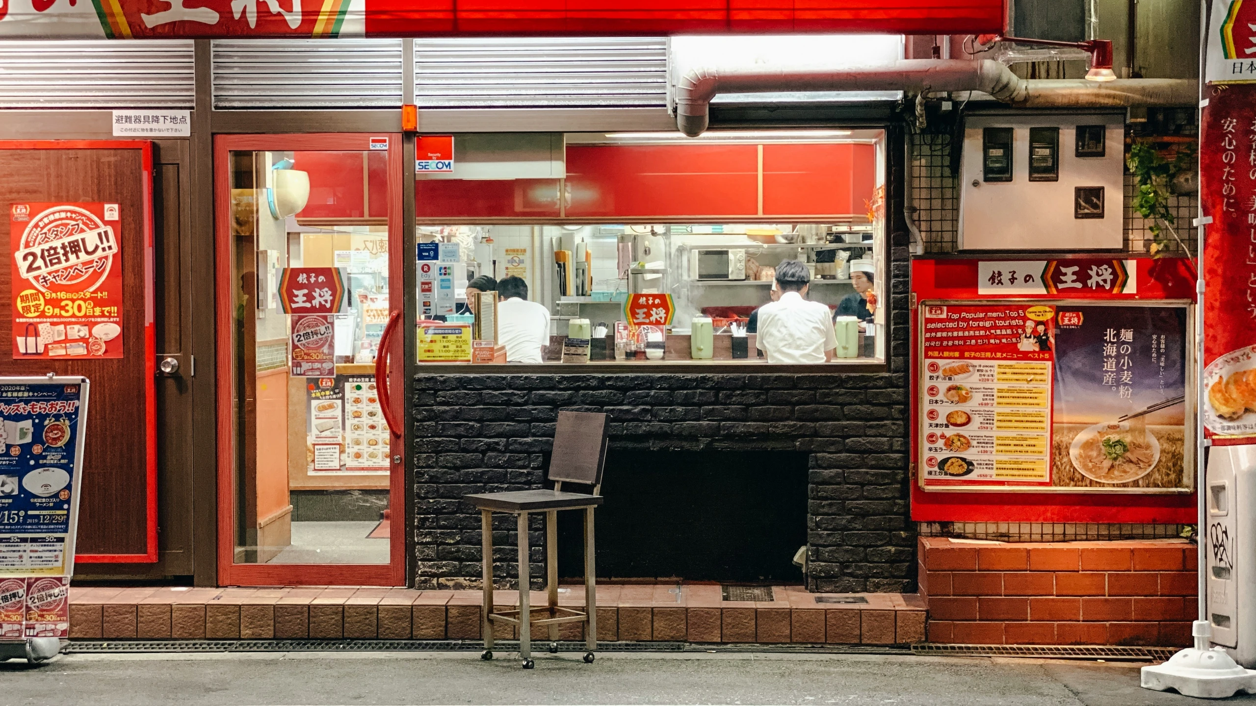 a restaurant with a menu window, a small stool on the sidewalk and some red signs