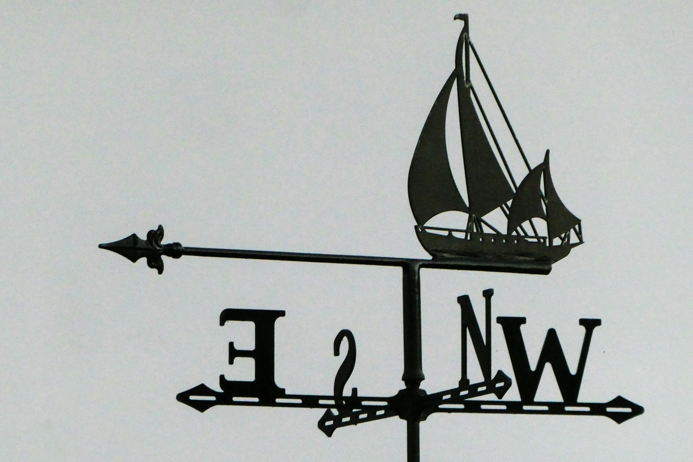 a wind vane on a metal pole with a boat on it