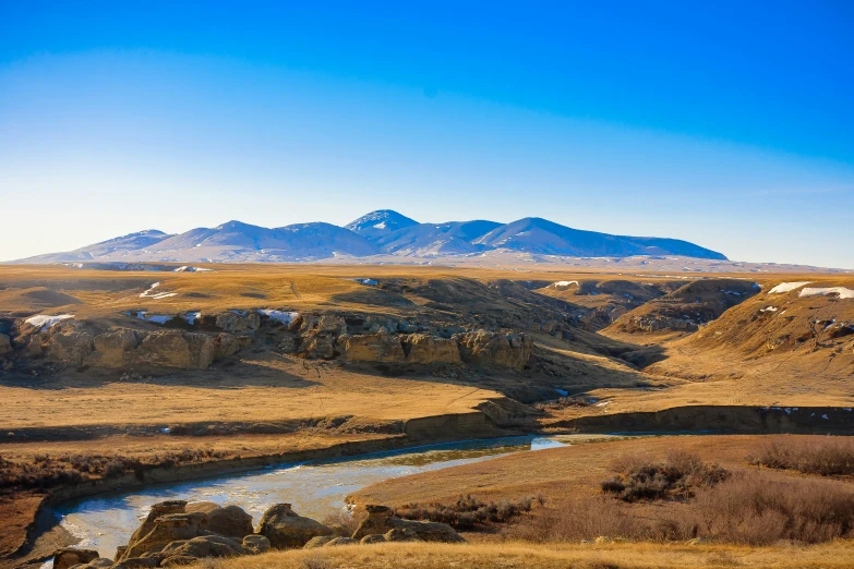 a river in a dry field with mountains in the background