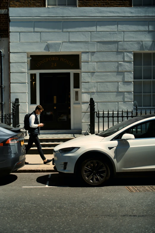 the man crosses the street next to cars as they are stopped on the sidewalk