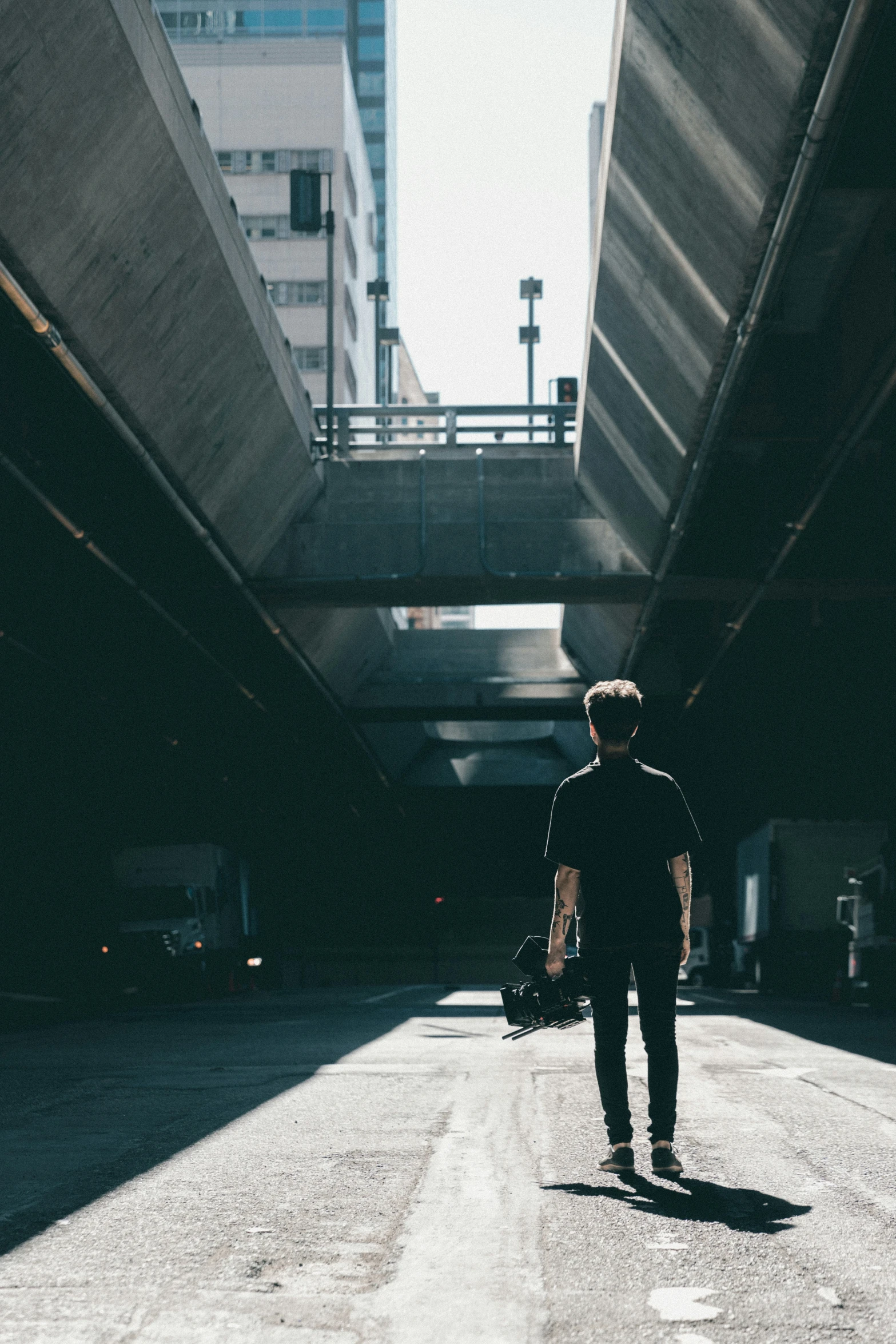 man holding luggage walking under a freeway overpass