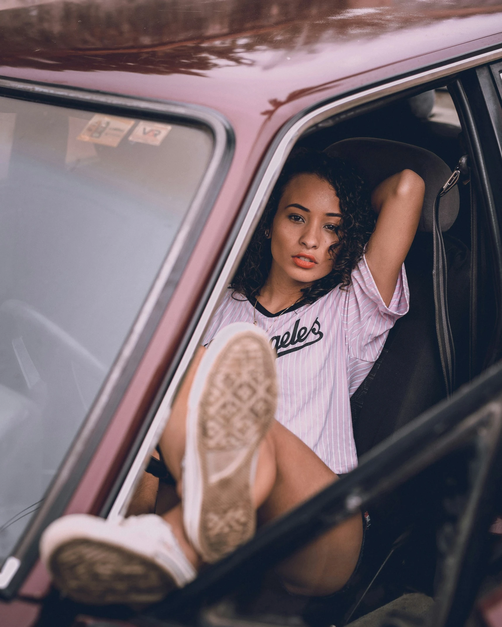 a young woman leaning out the window of a pink car