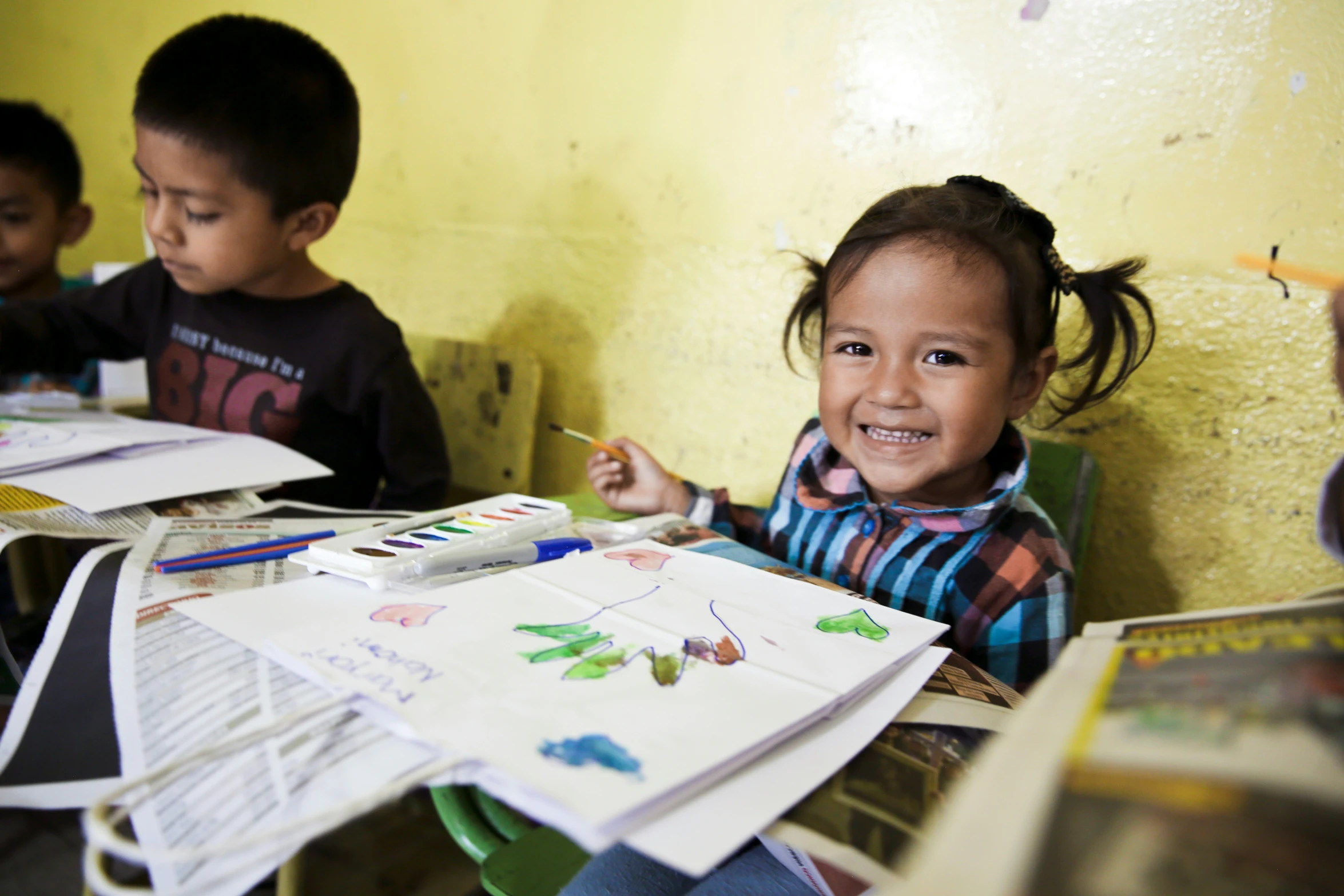 two children sit in a room with books and paper